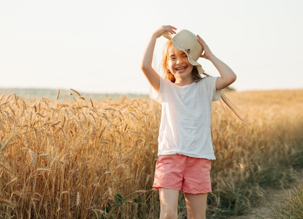 kid girl with hat, happy smiles beautifully while in golden wheat field