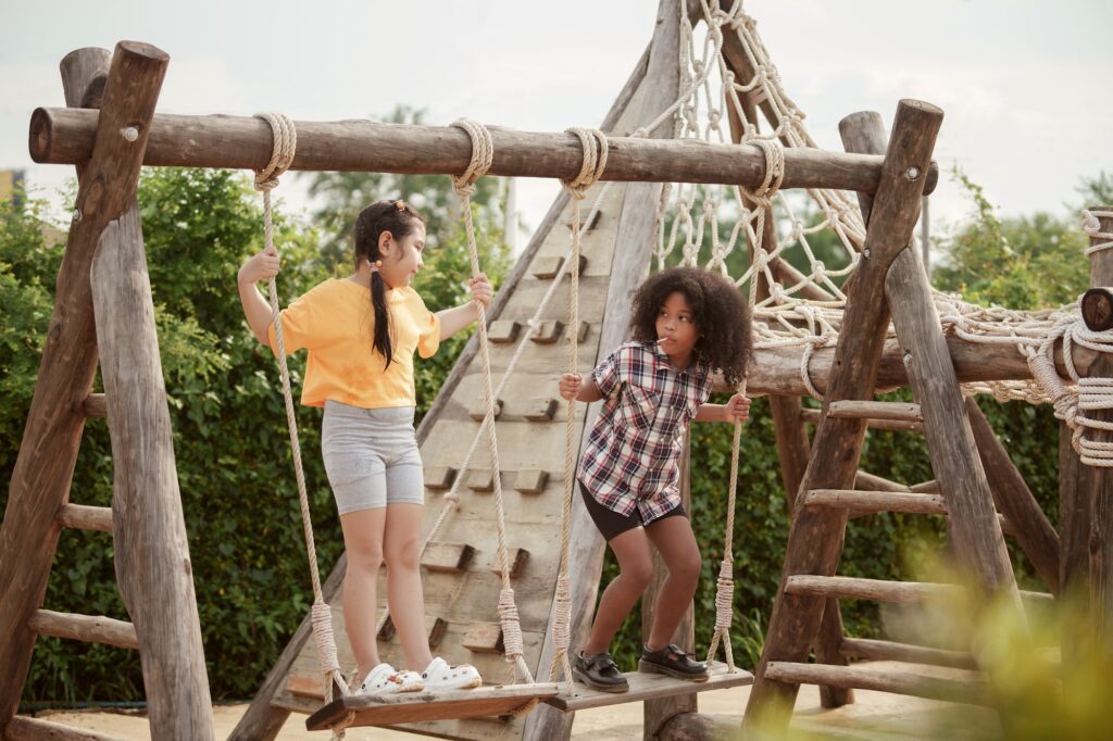 Two kids girl are playing on the swing in the outdoor playground.