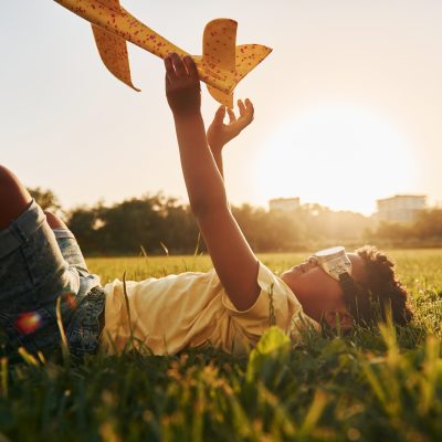 Boy with toy plane. African american kid have fun in the field at summer daytime